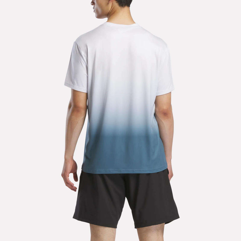 A man wears the Reebok Men's Athlete Speed Ombré T-Shirt, featuring a white-to-blue gradient and short sleeves, paired with black shorts. He faces away to display the back, set against a plain white background.