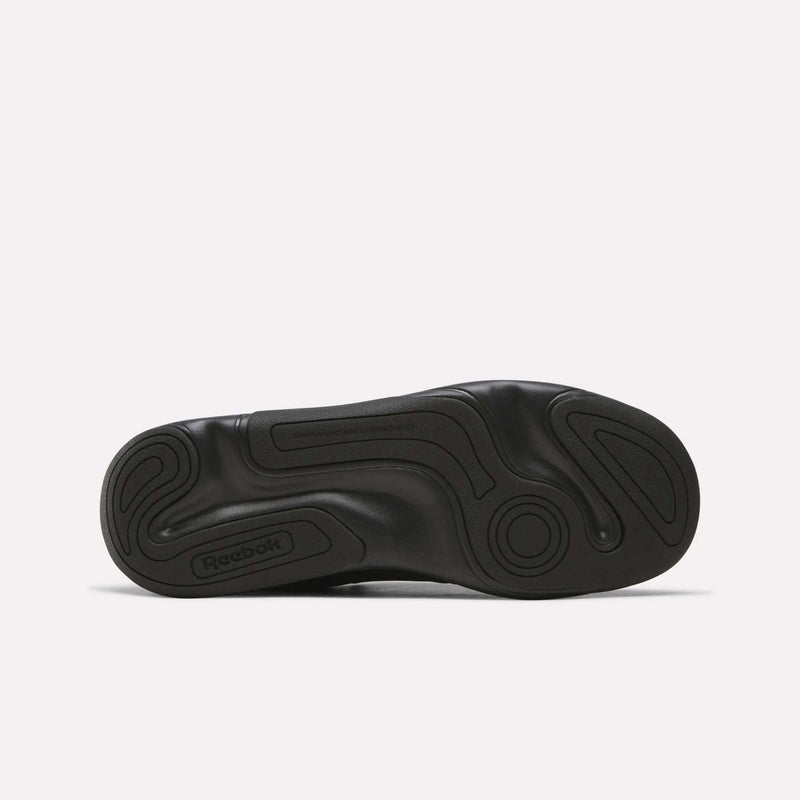 The bottom view of the DMX Comfort+ Classic walking shoe sole from Reebok reveals a black, wavy, textured grip pattern. Designed specifically for walking shoes, this sole incorporates Dynamic air cushioning for superior comfort. An embossed Reebok logo is visible near the heel against a plain white background.
