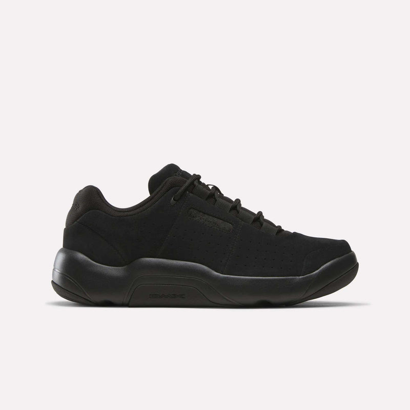 Introducing the Reebok DMX Comfort+ Classic, a black low-top sneaker crafted from premium leather. Featuring a thick sole, lace-up closure, and subtle side perforations for breathability, these shoes are designed with all-day walking comfort in mind. Shown here in Black/Black/Black, displayed in side profile against a plain white background.