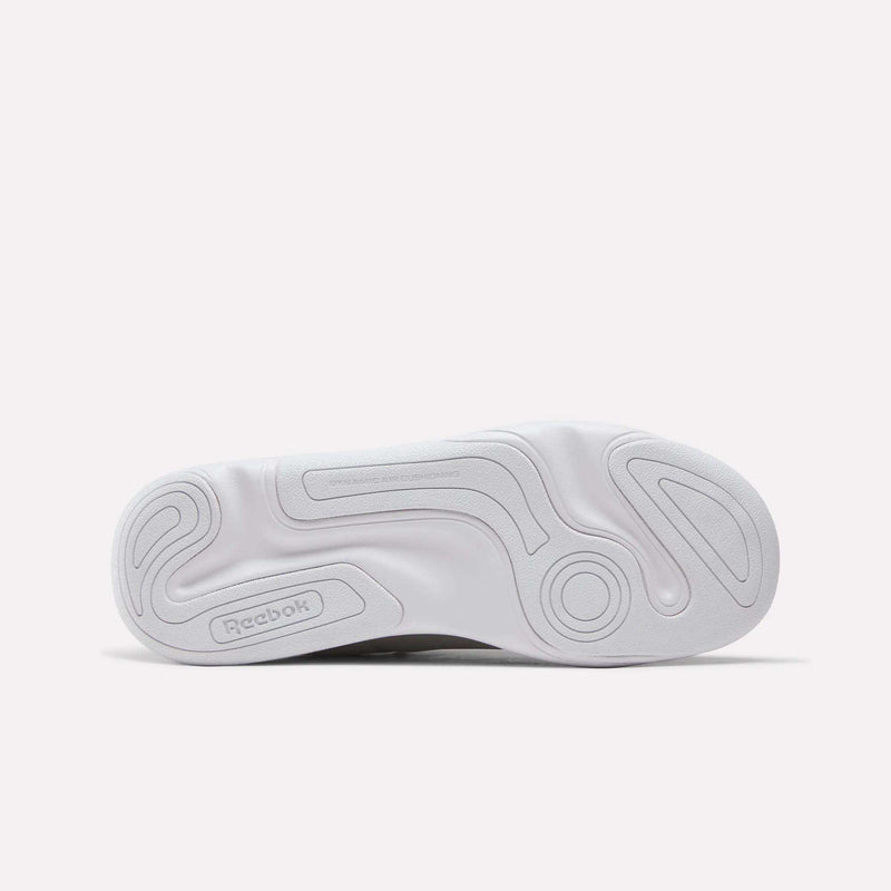 The image displays the white rubber outsole of the Reebok DMX Comfort+ Classic sneaker, featuring wavy textured patterns and an embossed Reebok logo on the heel, emphasizing its reliability as a walking shoe.
