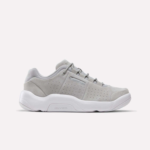 The Reebok DMX Comfort+ Classic sneaker, showcased in a side profile against a plain white background, features a New Grey 2 suede upper with perforated sides, premium leather accents, crisp white laces, and a thick white sole equipped with dynamic air cushioning.