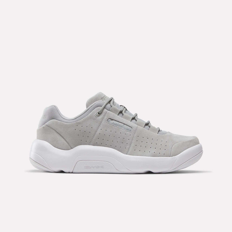 The Reebok DMX Comfort+ Classic sneaker, showcased in a side profile against a plain white background, features a New Grey 2 suede upper with perforated sides, premium leather accents, crisp white laces, and a thick white sole equipped with dynamic air cushioning.