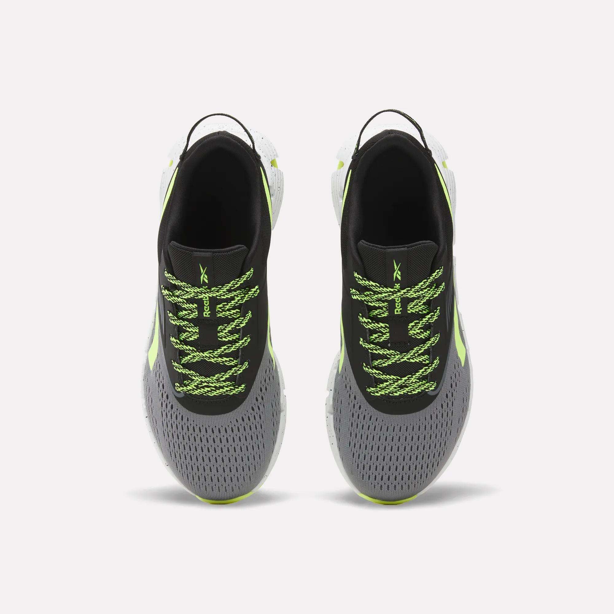 A pair of Reebok Zig Dynamica 6 Running Shoes for big kids, in gray with black interiors, neon green patterned laces, Zig technology soles, and light green accents, displayed from above on a plain white background.