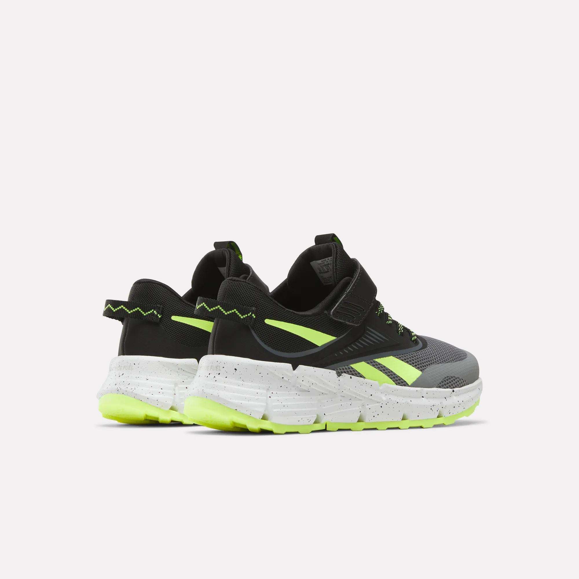A pair of Reebok Zig Dynamica 6 Running Shoes for little kids in black and gray with neon yellow accents, Zig technology, white speckled soles, and chunky neon outsoles, shown on a plain white background.
