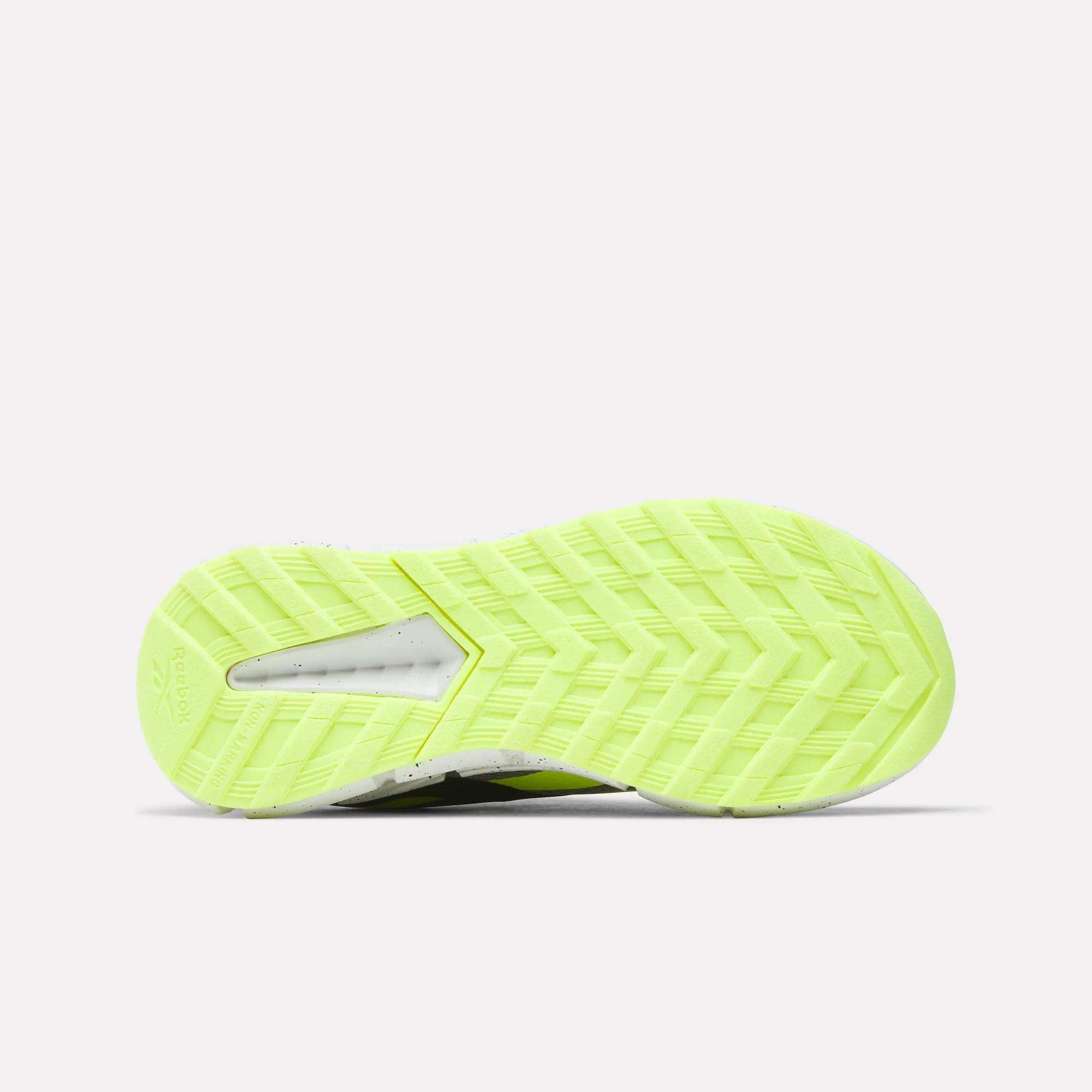 The image shows the sole of the Reebok Zig Dynamica 6 Running Shoes for little kids in bright yellow-green, with a herringbone tread pattern and a small translucent heel window highlighting Zig technology.
