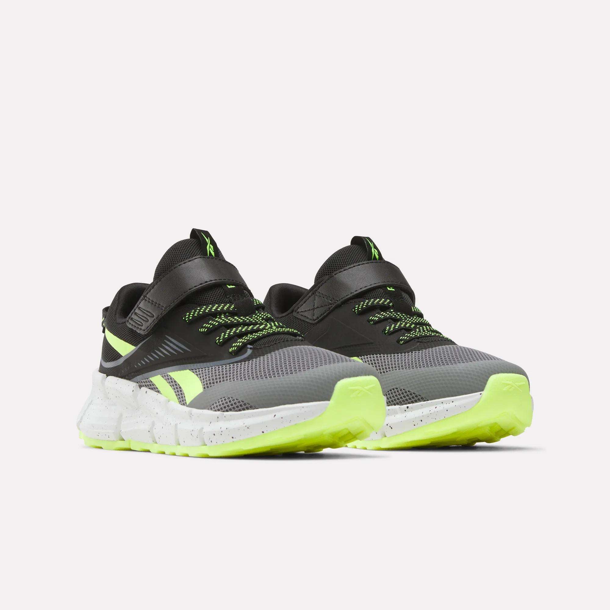 The Reebok Zig Dynamica 6 Running Shoes for little kids feature a black and gray design with neon green accents, green-tipped laces, and speckled white soles, displayed on a light background.