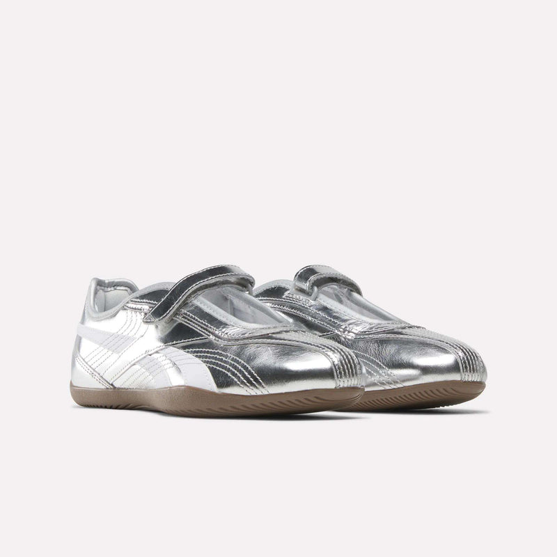 A pair of Reebok Women’s Ultra Lo Mary Jane shoes in silver and white, featuring Velcro straps and gum rubber soles, displayed on a plain white background.