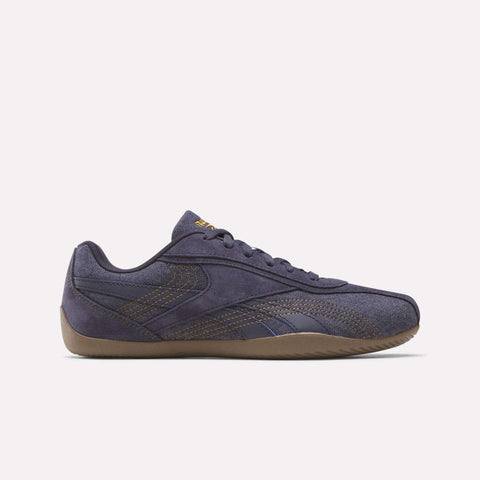 The Women's Ultra Lo Shoes by Reebok in Darkindigo/Reeboklee2 are showcased in side profile against a white background, featuring brown stitching, a gum-colored sole, and a low-top silhouette inspired by Reebok motorsport.