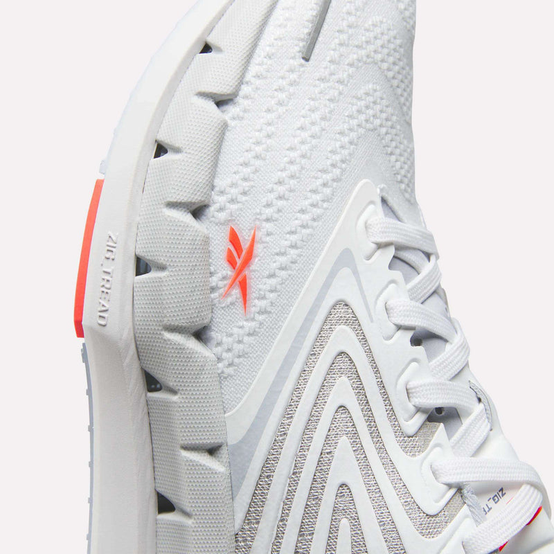 Close-up of Reebok Women's FloatZig Tread Running Shoe with breathable mesh, textured sole, gray curved patterns, white laces, and an orange logo. “Zig Kinetica” and “Zig” are embossed near the heel on the sole.