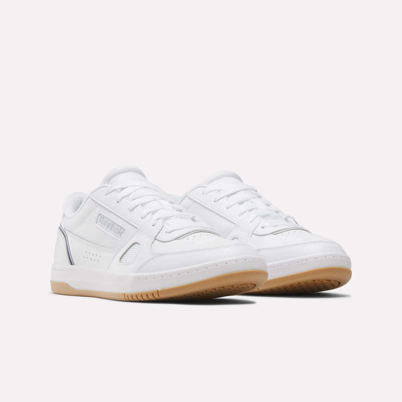 Introducing the Men’s Court LXS Shoes by Reebok: These white low-top sneakers are crafted from premium full-grain leather and feature gum rubber soles, crisp white laces, and subtle silver accents. Shown against a plain light background, they offer a modern, elevated spin on classic men’s court footwear.