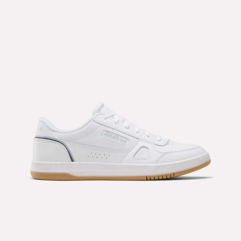The Reebok Men’s Court LXS Shoes in White/Legacyblue/Grey1 feature a premium full grain leather construction, low-top silhouette, lace-up closure, perforated side detailing, and a light brown rubber sole. Displayed in side profile against a plain light background, these men’s court shoes by Reebok offer an effortless blend of style and comfort.