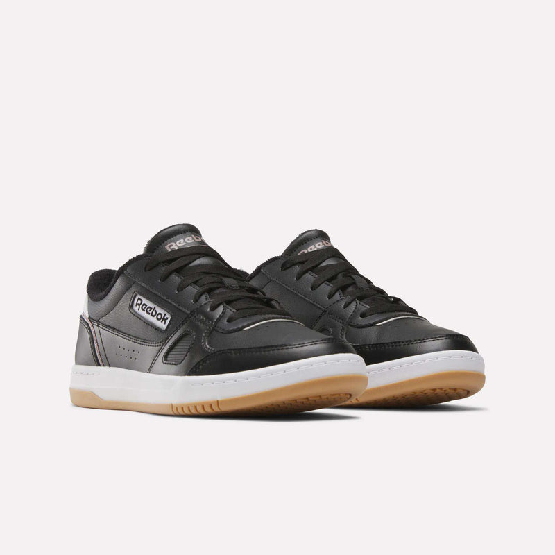 A pair of Men’s Court LXS Shoes by Reebok in black, crafted from premium full grain leather with white midsoles, gum outsoles, and silver Reebok logos on the sides and tongues, are showcased against a plain white background—designed as stylish men’s court shoes.