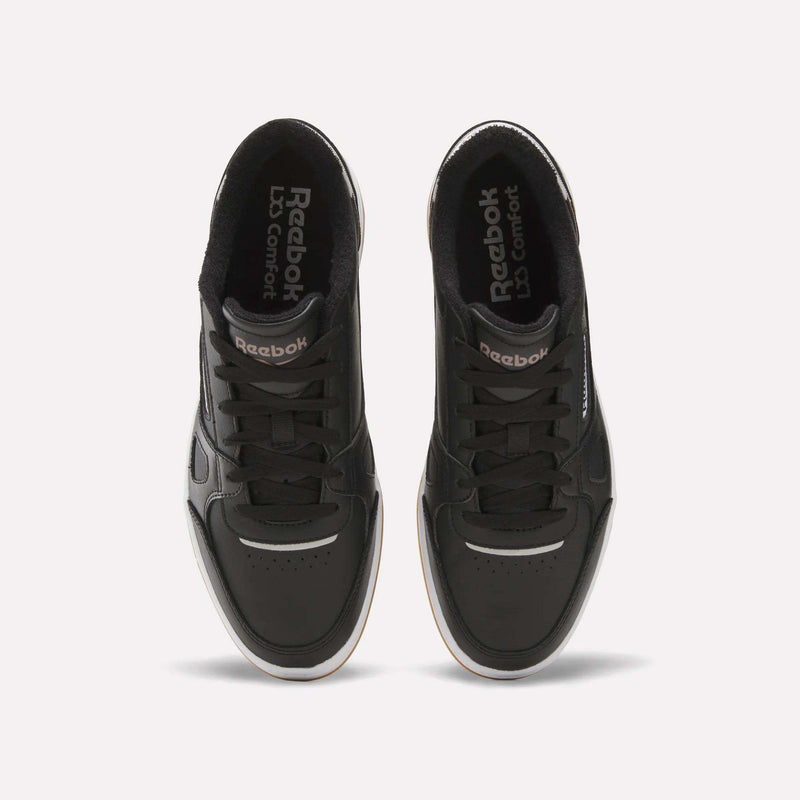 A pair of Reebok Men’s Court LXS Shoes in black, made from full grain leather, are shown from above with visible laces, perforated toe boxes, and Reebok branding on the tongues. The shoes feature white midsoles and are positioned side by side on a plain background.
