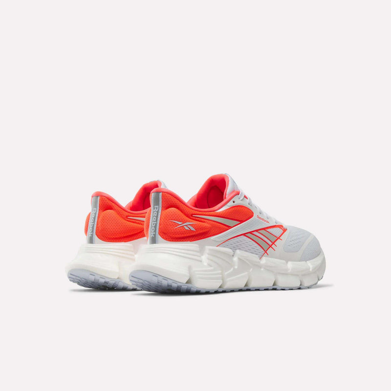 A pair of Women's FloatZig 2 Running Shoes by Reebok in white and orange, displayed from the back and side, featuring thick white Superfloat+ cushioned soles for a springy feel, silver accents, and the Reebok logo on the side and heel tab.
