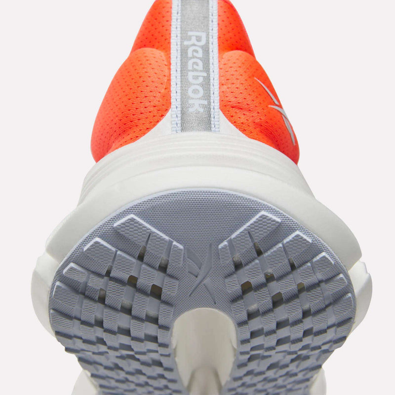 Close-up view of the sole and heel of a red and white Women's FloatZig 2 Running Shoe by Reebok, showcasing textured grip patterns, Superfloat+ cushioning for enhanced comfort, and the Reebok logo displayed on the back.
