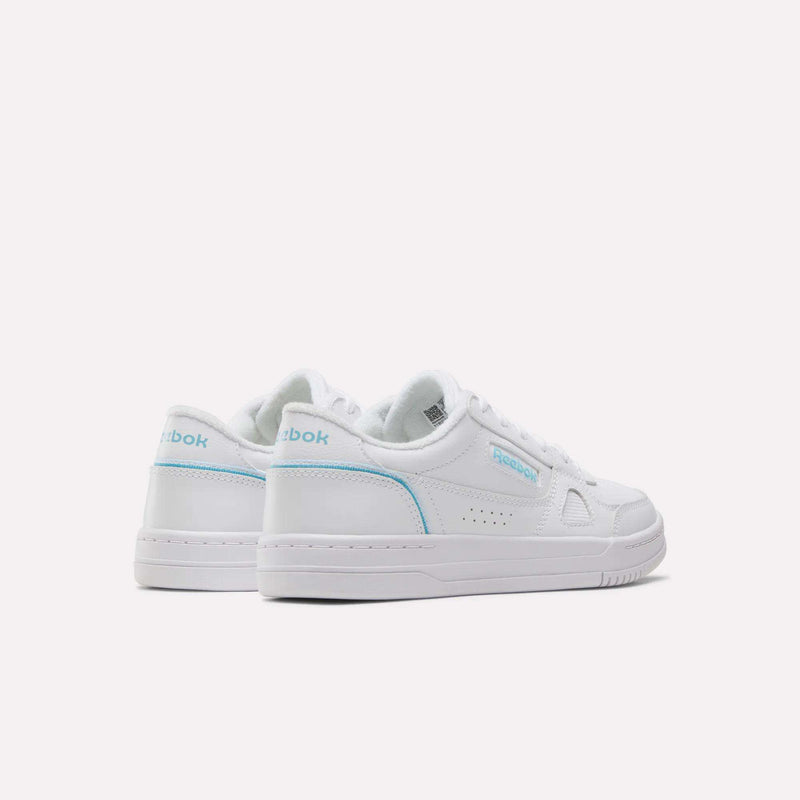 A pair of white Reebok Women’s Court LXS Shoes crafted from full grain leather with light blue accents is displayed on a plain light background. One shoe faces backward while the other faces forward, showcasing both the heel and side views of these women’s court shoes.