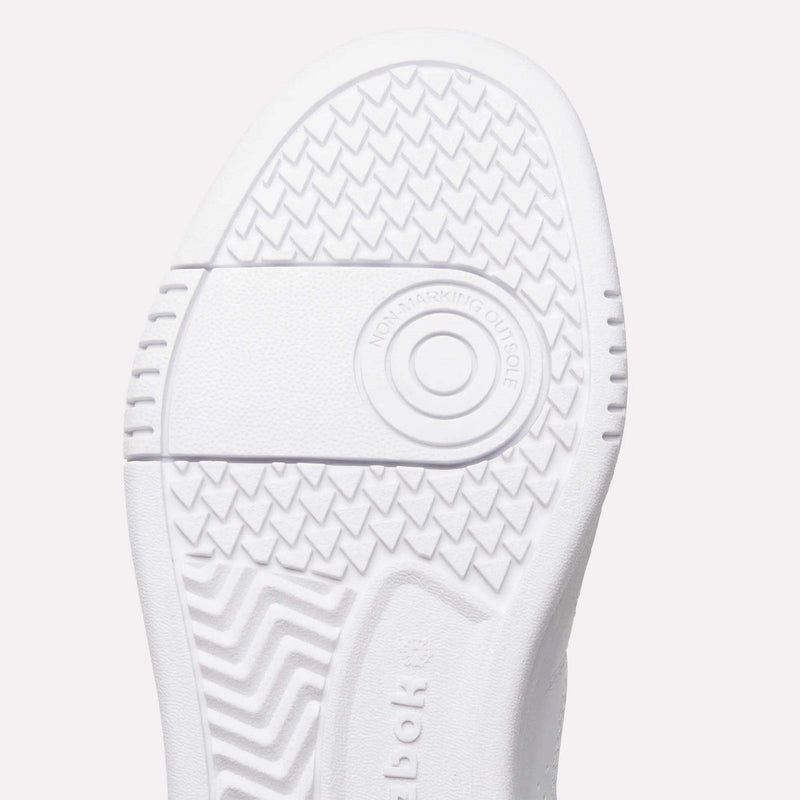 Close-up of the white sole of Reebok Women’s Court LXS Shoes, a premium choice in women’s court shoes, featuring zigzag and circular tread patterns. Crafted with full grain leather, the words NON-MARKING OUTSOLE are visible inside a ring near the center.