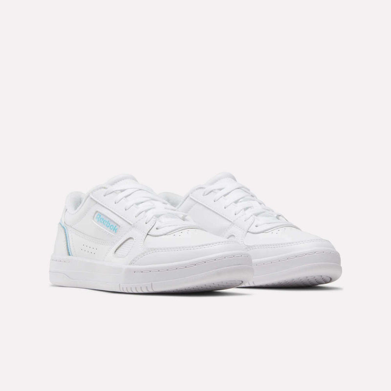 A pair of white Reebok Women’s Court LXS Shoes with light blue accents, crafted from premium full grain leather, displayed on a plain white background and positioned at a slight angle to showcase the side and front of these classic women’s court shoes.