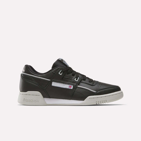 The Reebok Workout Plus Shoes are black leather low-tops with a white sole and subtle white and gray accents. Stylish for workouts, they display the Reebok logo and flag on the side.