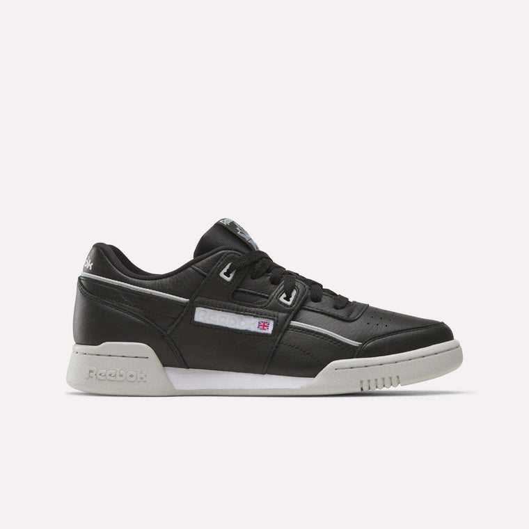 The Reebok Workout Plus Shoes are black leather low-tops with a white sole and subtle white and gray accents. Stylish for workouts, they display the Reebok logo and flag on the side.