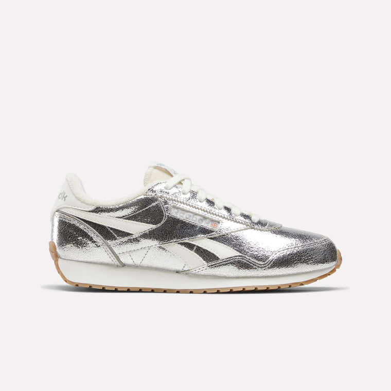 A pair of Reebok Women’s Classic AZ Shoes in Silver/Chalk/Gum, featuring a metallic silver upper with white laces and cream accents, are displayed against a plain light background.