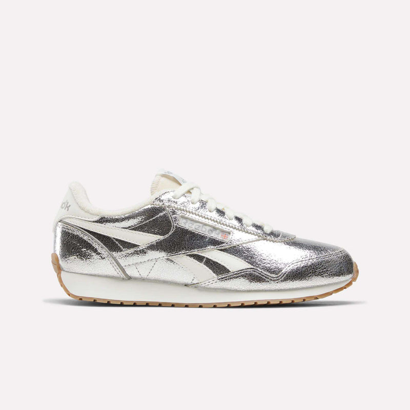 A pair of Reebok Women’s Classic AZ Shoes in Silver/Chalk/Gum, featuring a metallic silver upper with white laces and cream accents, are displayed against a plain light background.