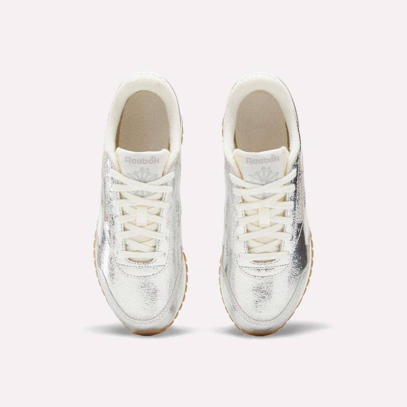 A pair of Women’s Classic AZ Shoes by Reebok in white and silver, viewed from above, featuring cream-colored laces and light brown outsoles—these retro running shoes seamlessly combine timeless style with contemporary metallic details.