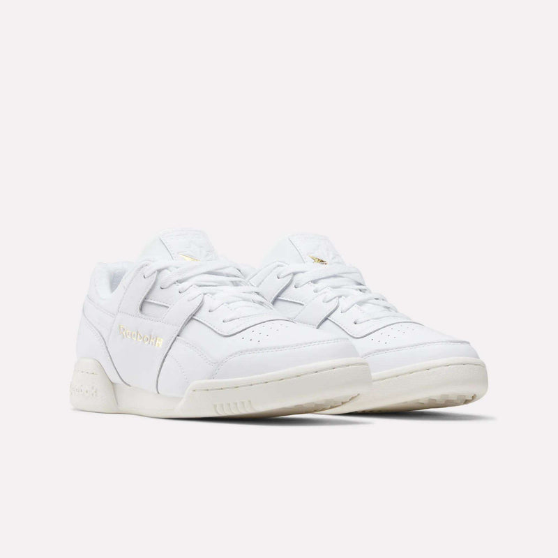 A pair of Reebok Workout Plus Shoes with gold branding, white laces, and off-white soles are displayed on a plain light background, capturing the classic '80s fitness style.
