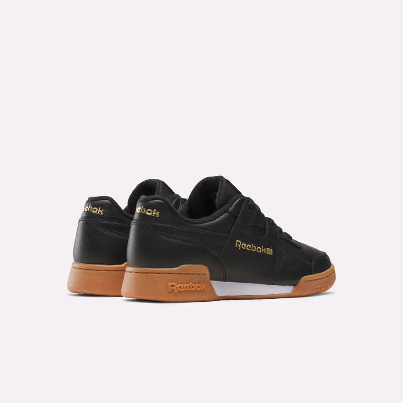 A pair of Reebok Workout Plus Shoes in black with brown gum soles and gold Reebok logos on the heel and side, channeling iconic ’80s fitness style, displayed against a plain white background.