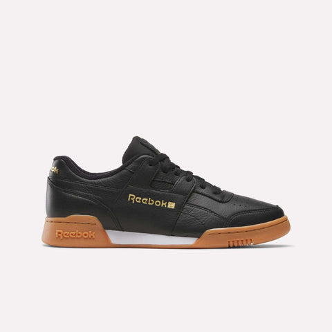 A side-profile of the Reebok Workout Plus Shoes in Black/Gold/Gum is displayed against a plain white background, featuring gold Reebok branding on the side and heel, black laces, and a classic gum sole—showcasing timeless ’80s fitness style.
