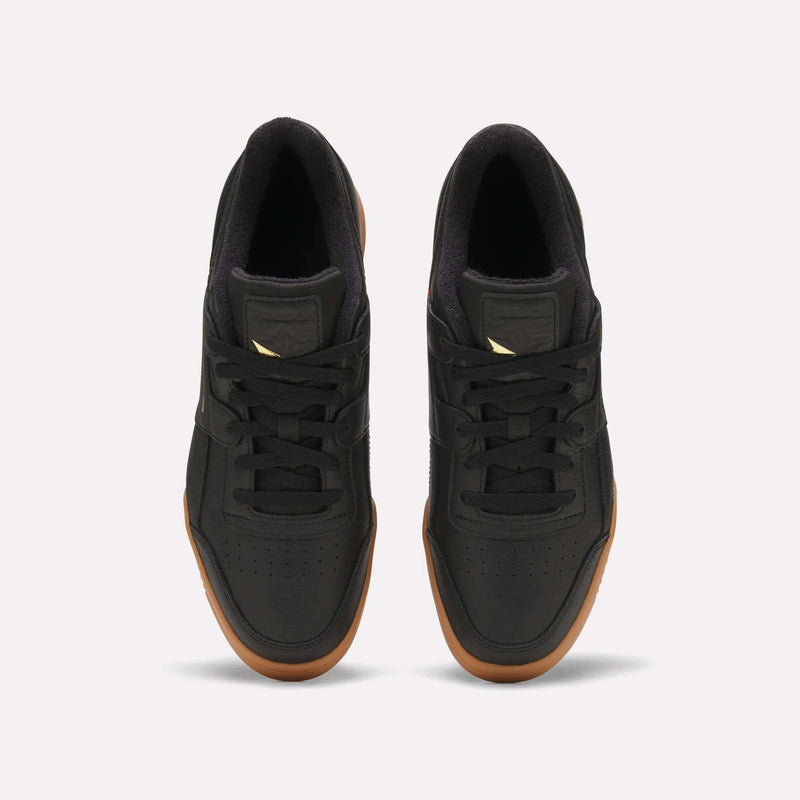 A pair of Reebok Workout Plus Shoes in black with gum soles, seen from above on a white background. Featuring black laces and a small gold Reebok logo on the tongue, these shoes evoke subtle ’80s fitness style reminiscent of the classic era.