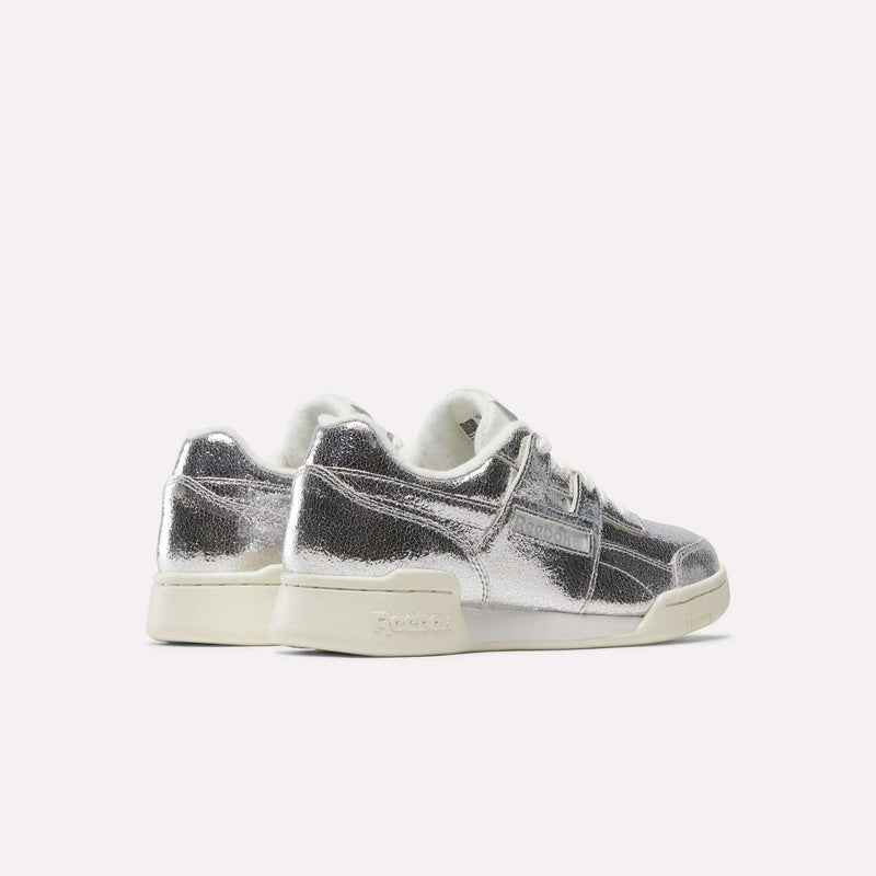 A pair of Reebok Women’s Workout Plus Shoes in silver metallic, made from premium garment leather, featuring white laces and off-white soles, displayed against a plain light background.