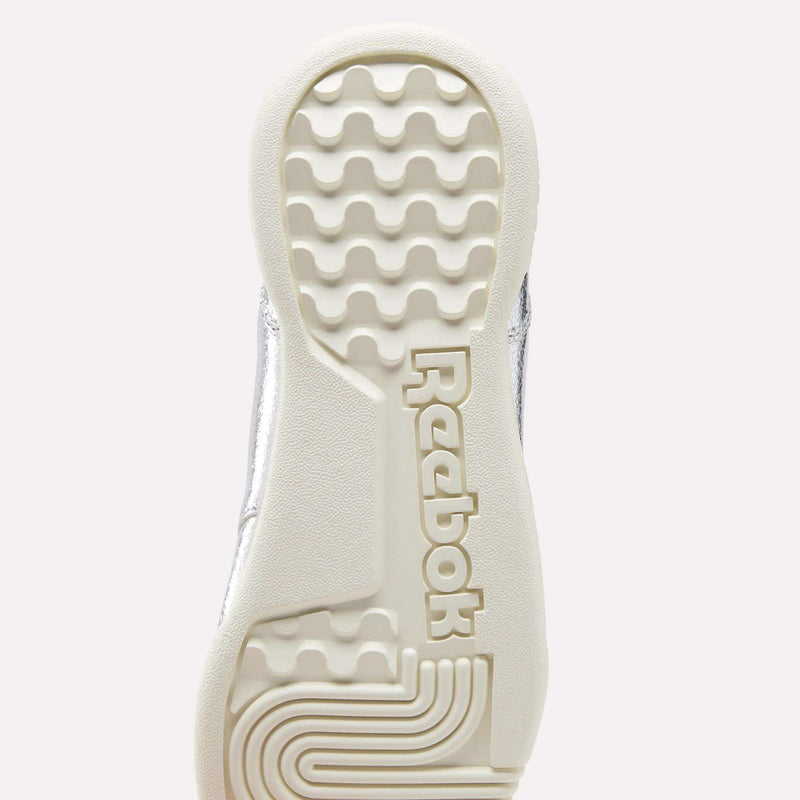 Certainly! Here’s a revised version of your sentence using the provided product data: The sole of a Reebok Women’s Workout Plus Shoe in white, viewed from below, displays the distinctive wavy tread pattern and the prominent raised Reebok logo at the center—an iconic sneaker designed with premium garment leather for enduring style and durability.