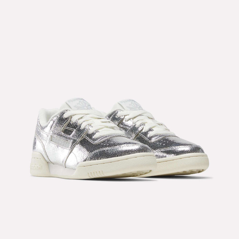 A pair of Reebok Women’s Workout Plus Shoes featuring shiny silver metallic premium garment leather uppers, white laces, and off-white soles are displayed on a plain white background—a modern update to the classic sneaker design.