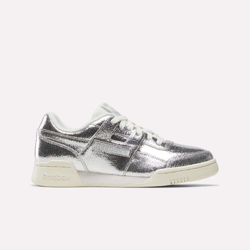 A pair of Reebok Women’s Workout Plus Shoes in Silver Metallic/Chalk/Vintage Chalk, crafted from premium garment leather with matching white laces and chalk-toned sole, shown from a side angle against a plain white background for a classic sneaker aesthetic.