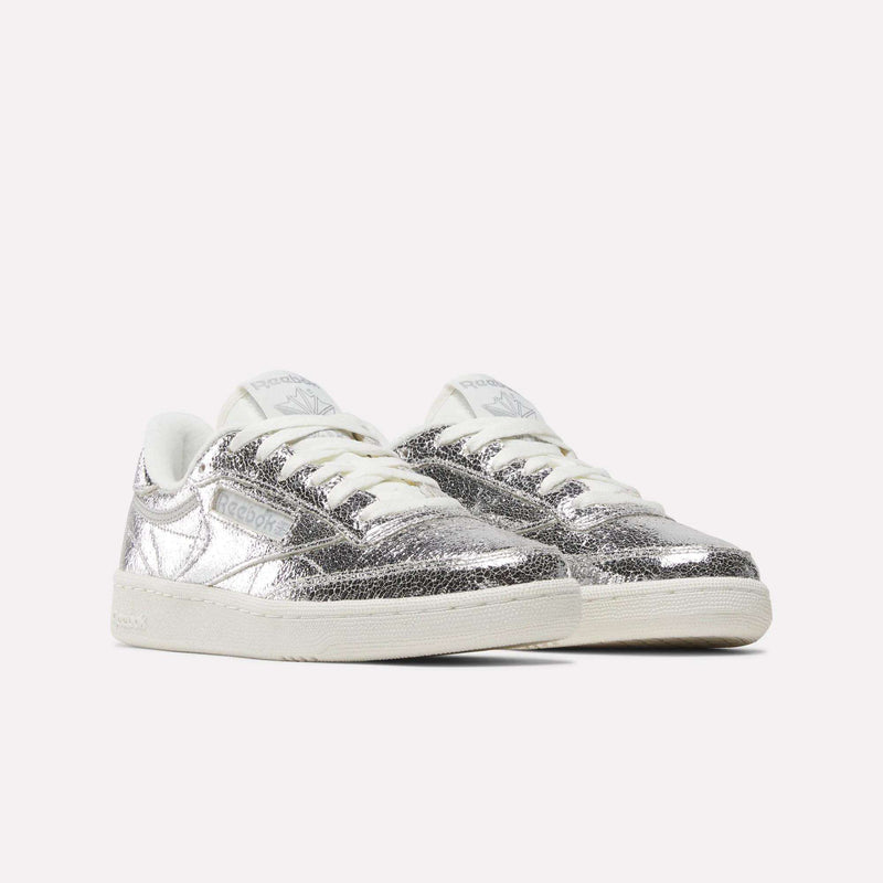 A pair of Reebok Women’s Club C 85 Shoes in metallic silver leather, featuring white soles and laces, displayed at a three-quarter angle against a plain light background.