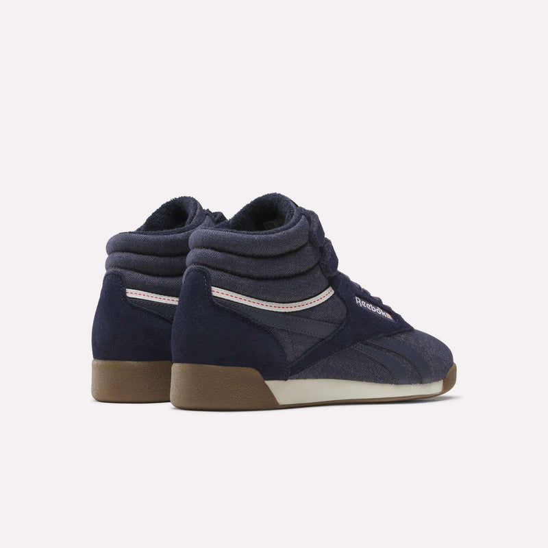 A pair of Women’s Freestyle Hi Shoes by Reebok in navy blue, featuring brown soles, white accents, and padded collars with a vintage denim-inspired look, displayed on a plain light background.