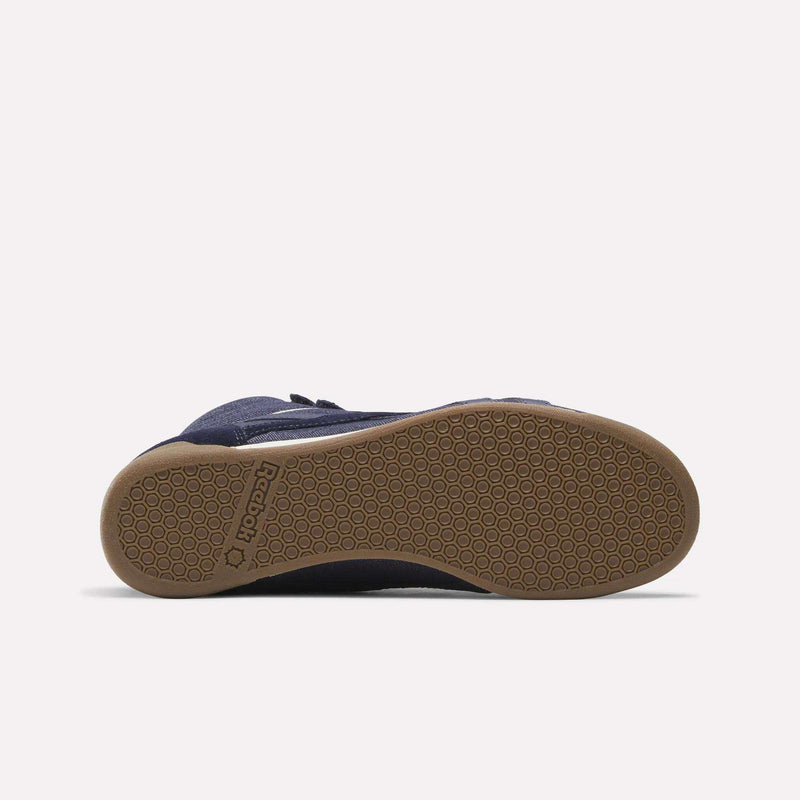 The Reebok Women’s Freestyle Hi Shoes are displayed from the sole, showcasing a navy blue upper with a light brown rubber outsole featuring a textured hexagonal pattern and Reebok branding near the heel.