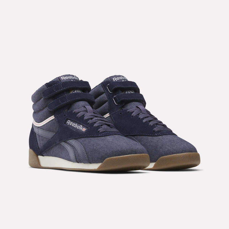 A pair of Women’s Freestyle Hi Shoes by Reebok in navy blue, featuring high-top design with velcro straps, suede and leather accents, white midsoles, and gum rubber outsoles, showcased against a plain white background for a classic Reebok appearance.