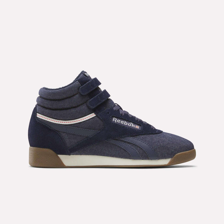 A pair of Reebok Women’s Freestyle Hi Shoes in Darkindigo/Chalk/Gum—a classic high-top silhouette featuring two velcro straps, a white midsole, a brown gum outsole, and pink accents—displayed against a plain light background.