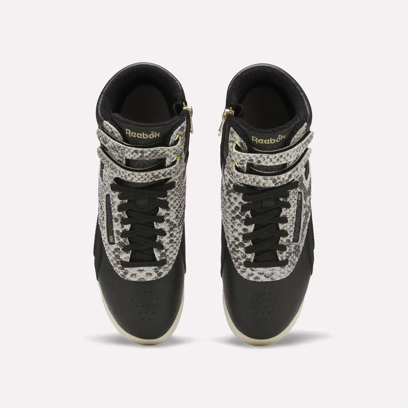 Top view of a pair of Reebok Women’s Freestyle Hi Zip Shoes in black, featuring white soles, black laces, and snakeskin-patterned accents on the straps and upper sides, displayed against a plain white background. These Reebok sneakers showcase an iconic retro women’s leather style with bold detailing for a standout look.