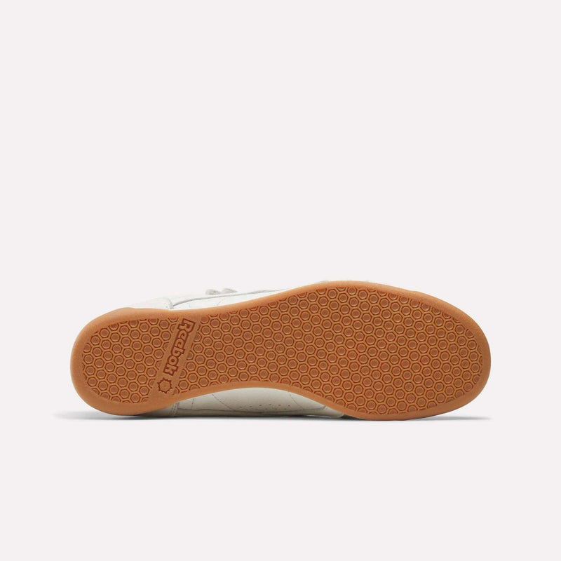The Women's Freestyle Hi Shoes by Reebok are displayed from the bottom, showcasing a textured gum rubber sole with hexagonal patterns and the Reebok logo imprinted near the heel against a plain white background.