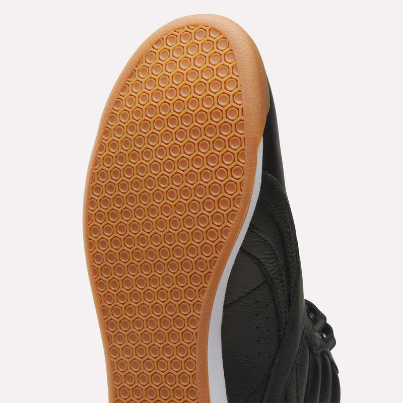 Bottom view of a black Reebok Women’s Freestyle Hi shoe, featuring a gum rubber outsole with a hexagonal tread pattern.