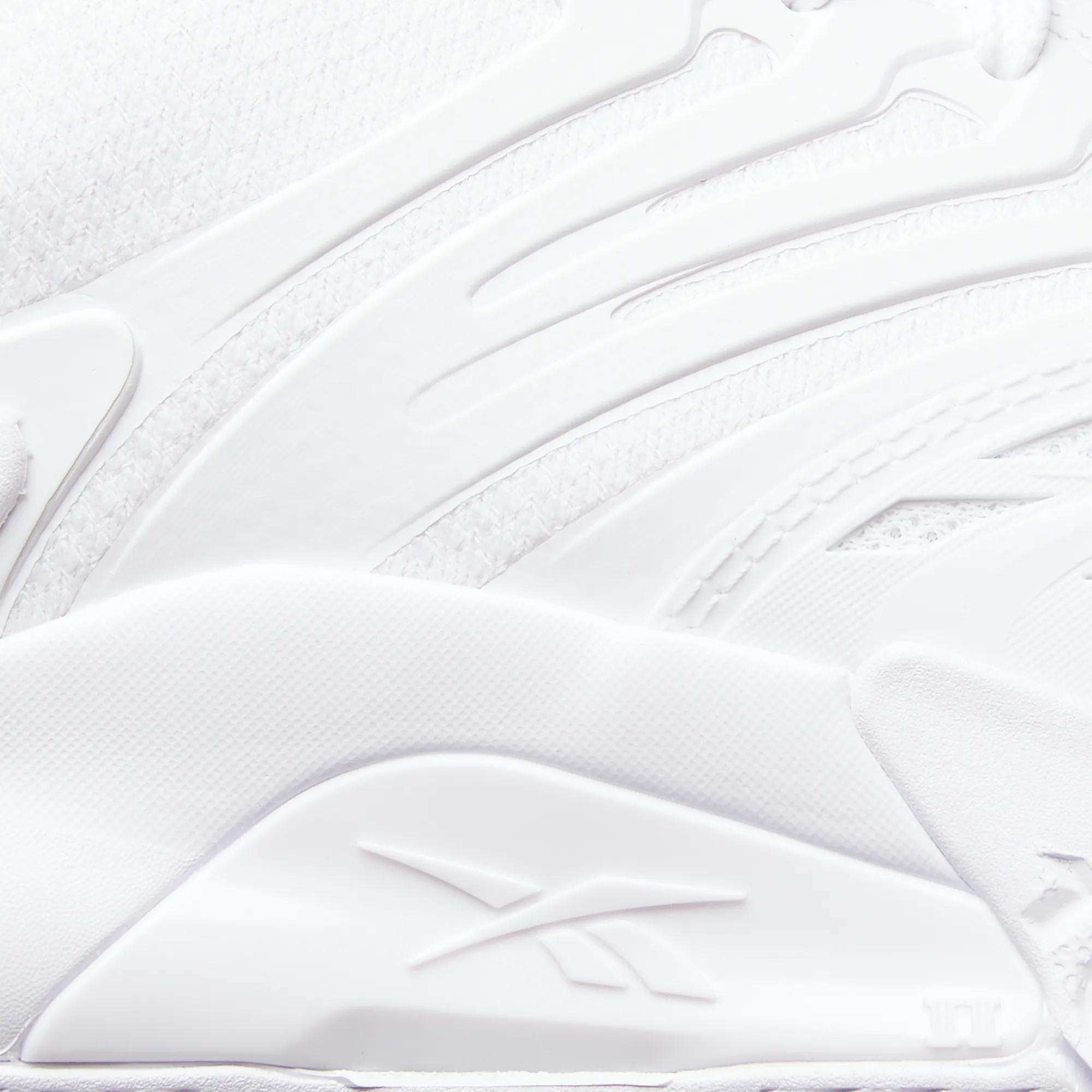 Close-up of a white Reebok Phase EVO Tennis Shoe, showcasing textured, layered materials and the embossed Reebok logo on the side. Smooth curves and raised patterns highlight its durable tennis shoe design.