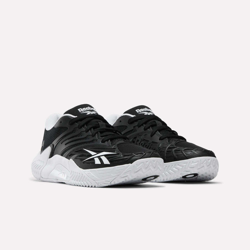 A pair of Reebok Women's Phase Evo Tennis Shoes with black uppers, white logos, white midsoles, and textured soles is displayed side by side on a light background.