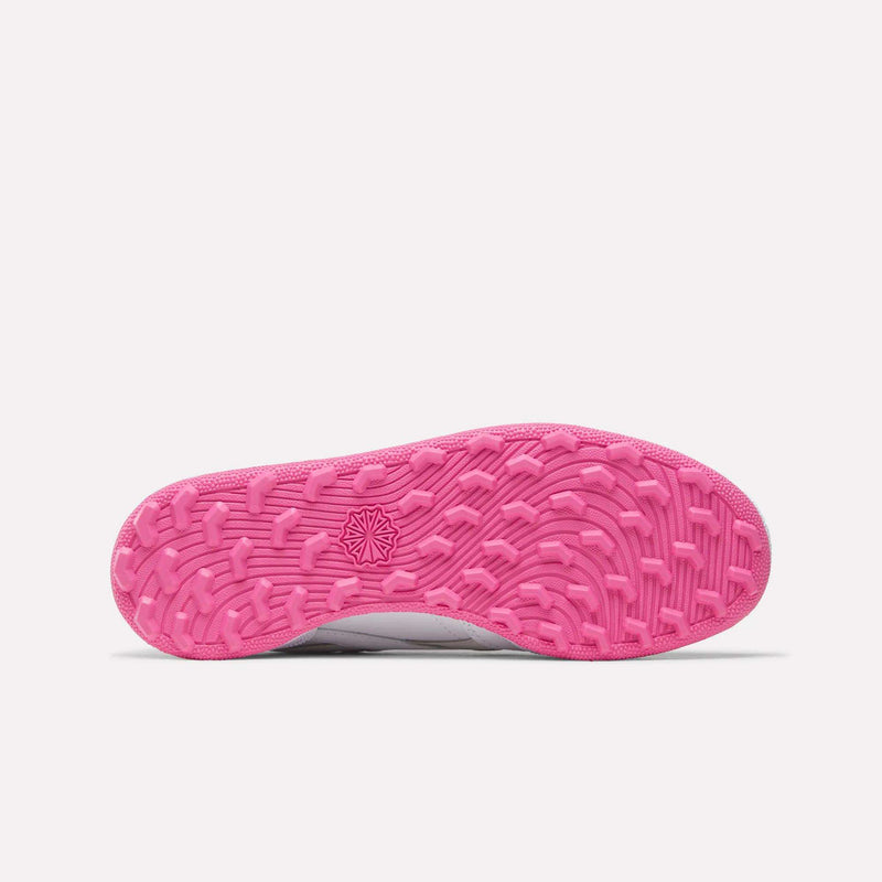 The image displays the bottom of the Reebok Women’s Club C Revenge Golf Shoes, featuring a vibrant pink, textured outsole with a wavy tread pattern and a small geometric Reebok logo in the center—an example of the stylish design typical of modern spikeless golf footwear.