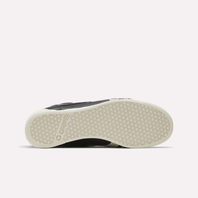 The image displays the sole of the Reebok Women’s Freestyle Lo Shoes in black, featuring a white, textured rubber outsole with a distinctive honeycomb pattern and an embossed Reebok logo near the heel. This classic style captures the signature quality and design of these women’s sneakers from Reebok.