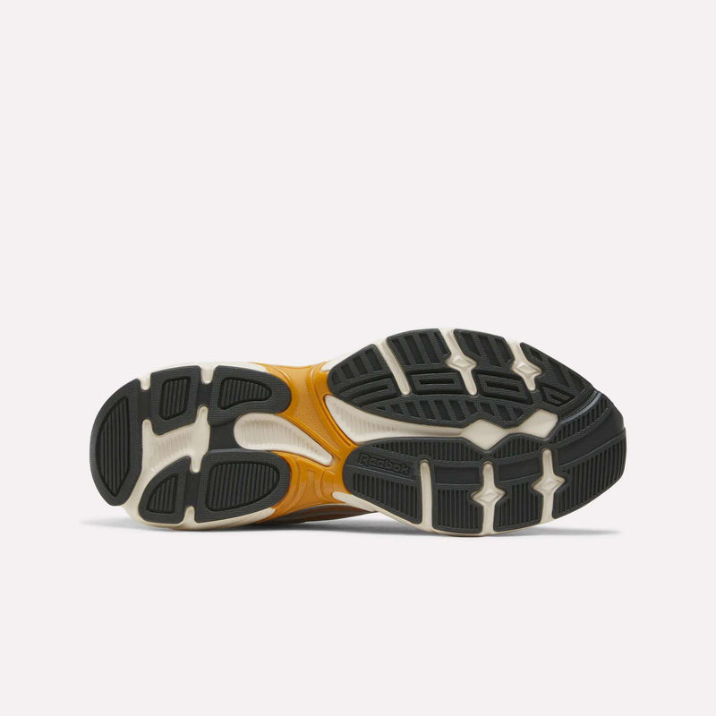 Bottom view of the Reebok Premier Road 1000 Shoes, showcasing a textured black and white rubber sole with orange accents and distinct tread patterns for grip and flexibility. Designed in true Y2K sneakers style by Reebok, these shoes also include an EVA midsole for enhanced comfort and support.