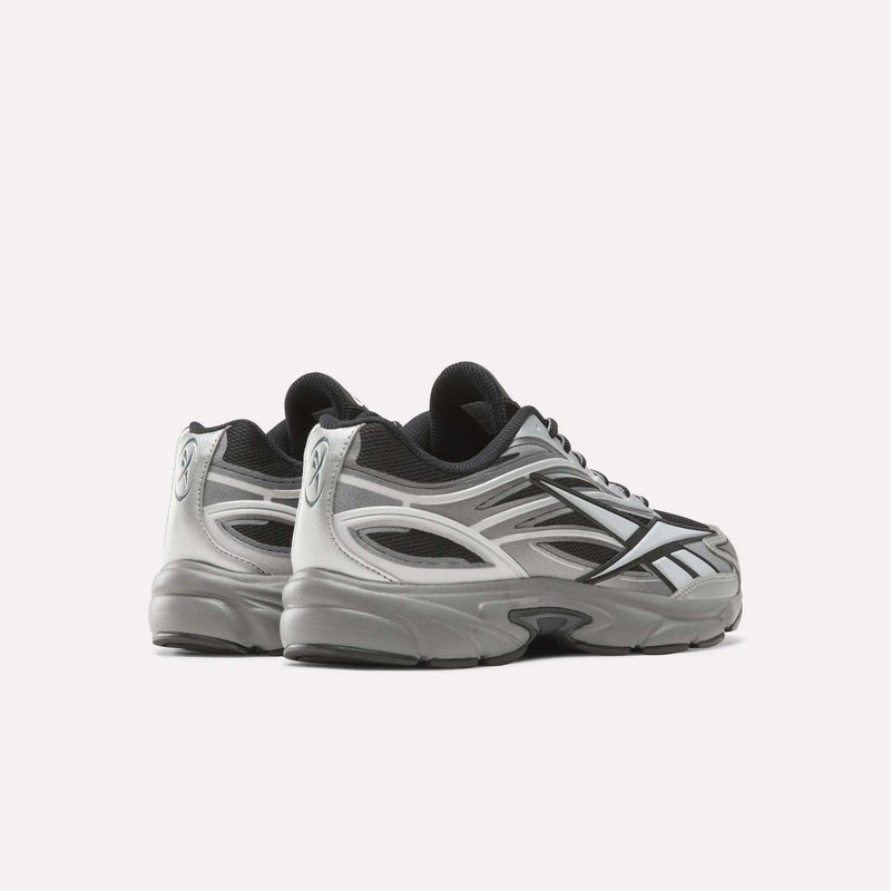 A pair of Reebok Premier Road 1000 Shoes in silver and black are displayed on a white background, showcasing the side and back details with visible mesh panels and reflective accents. Inspired by Y2K sneakers, these retro running shoes combine nostalgic style with modern performance elements.