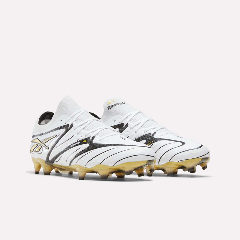 A pair of Reebok Sidewinder 26 Elite Firm Ground Cleats in white and gold with black accents, showcasing a modern design for superior ball control and molded stud soles optimized for firm grass, displayed on a plain white background.